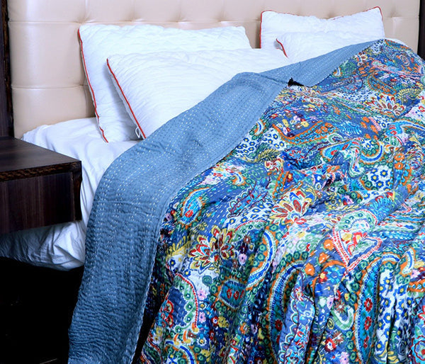 Colorful handmade Kantha quilt with intricate floral and paisley patterns draped on a bed with white pillows