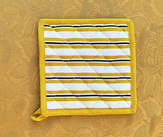 Quilted yellow and white striped cotton table linen pot holder on textured gold fabric background